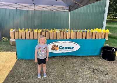Kid posing in front of Comer Construction table of loot bags at National Night Out