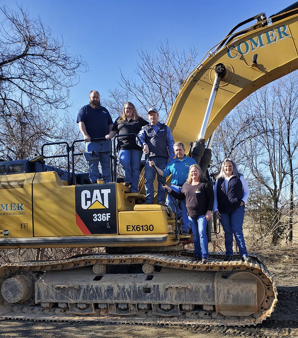 Leona and other family members standing on a Comer Construction excavator