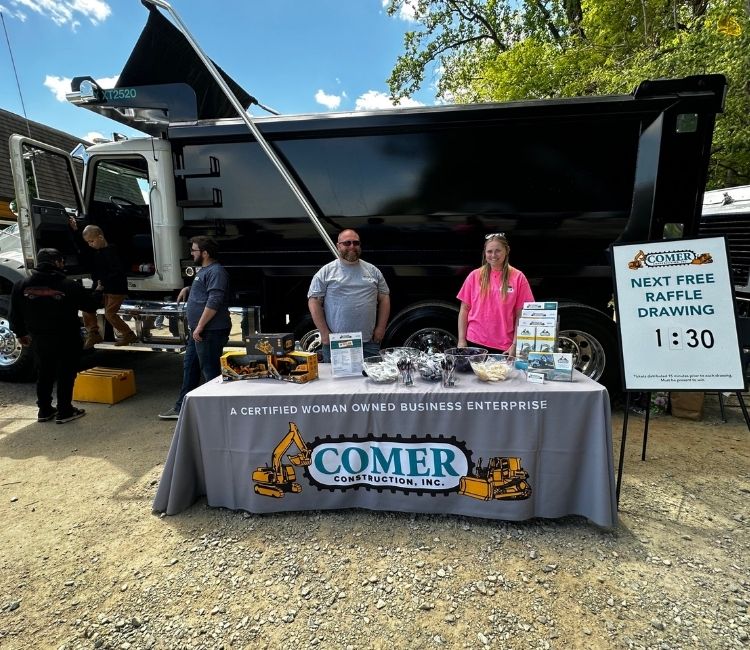 Comer Construction staff at a branded event table in front of a dump truck.