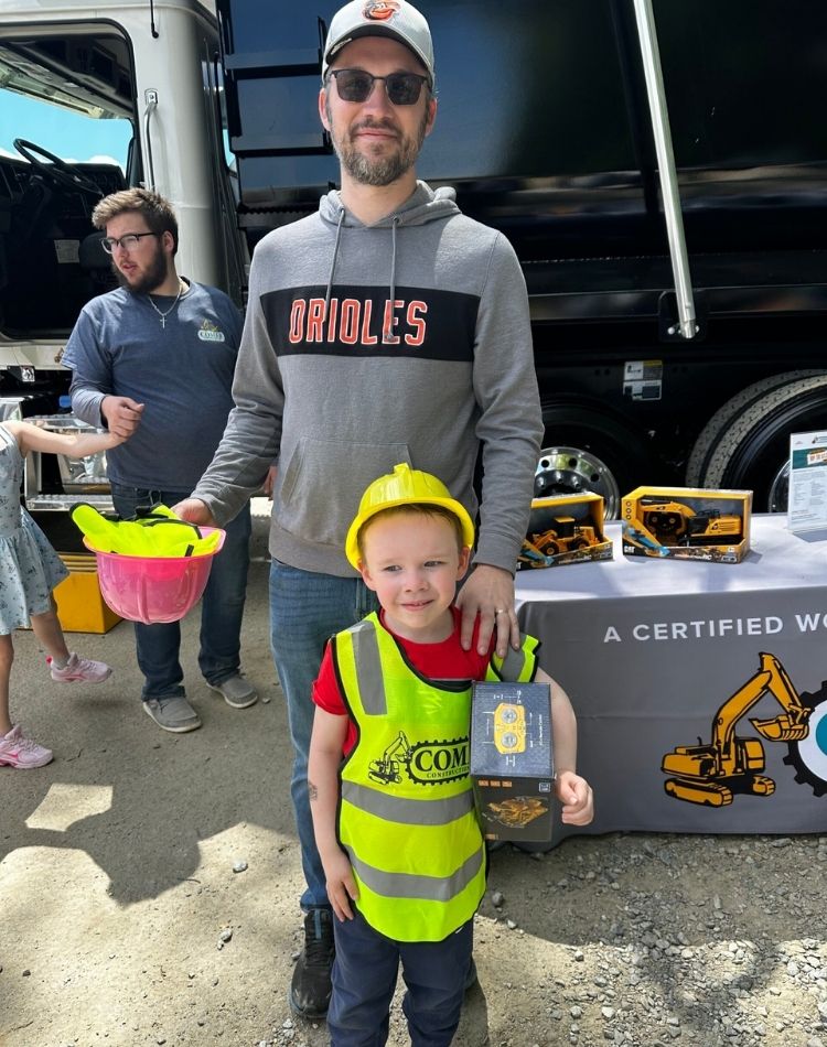A child and adult posing next to a small Comer Construction excavator.