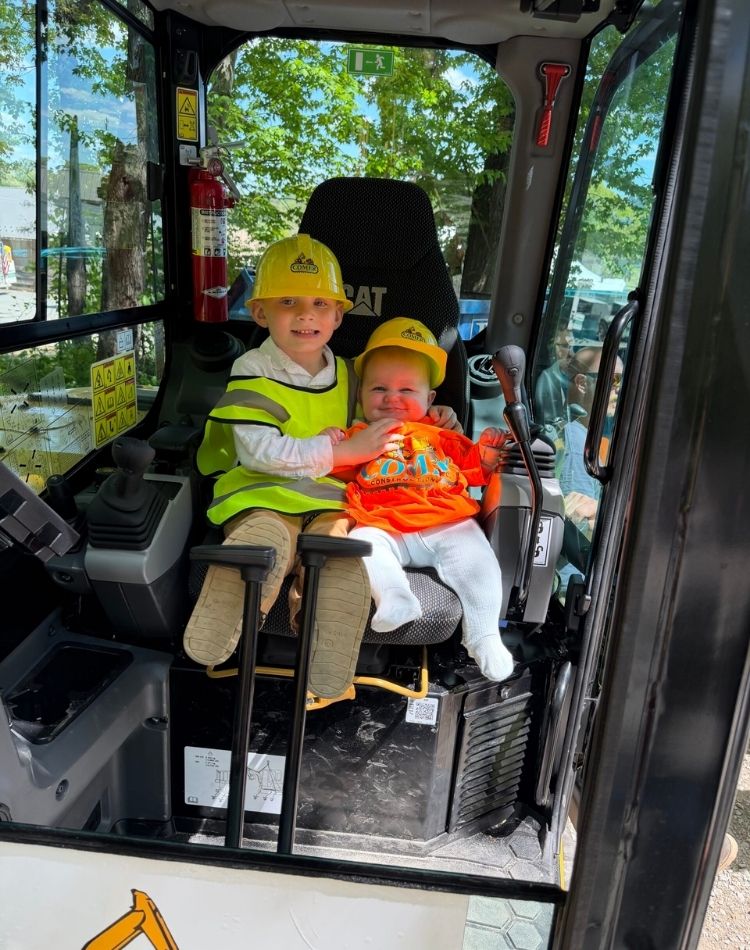 Two children sitting inside the cab of a Comer Construction machine.
