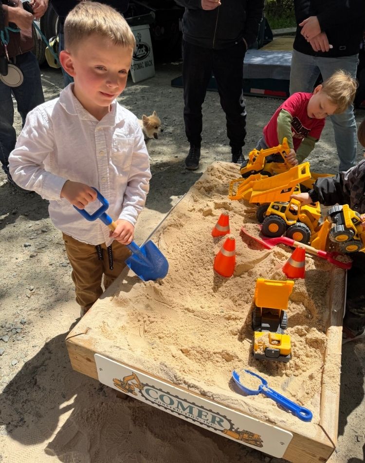 Children playing with toys in a Comer Construction branded sandbox.