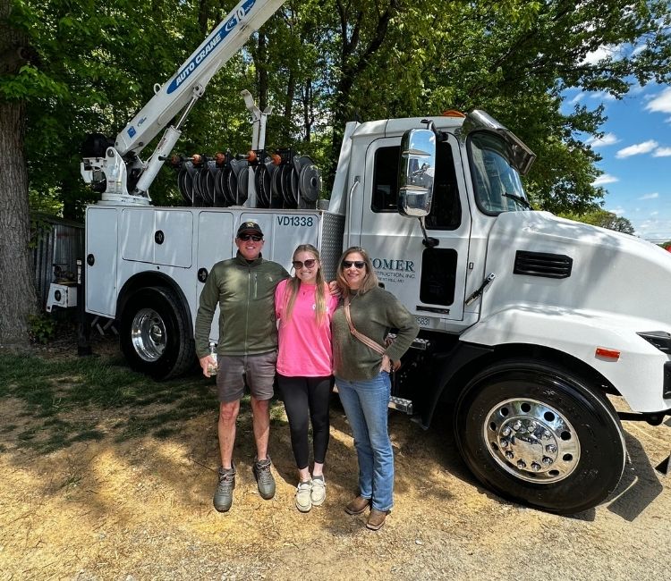 Three people standing in front of a Comer Construction utility truck.