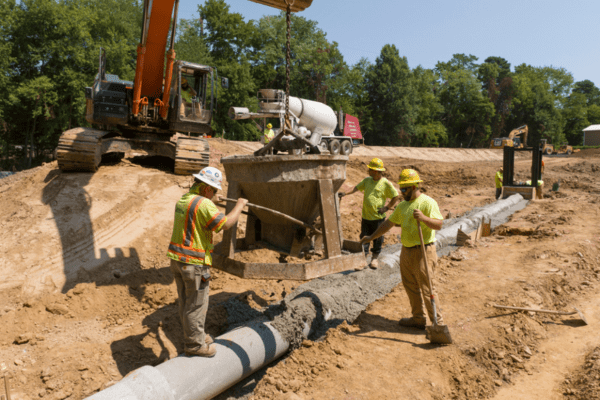 Crews pouring cement on top of a sewer pipe at a construction site