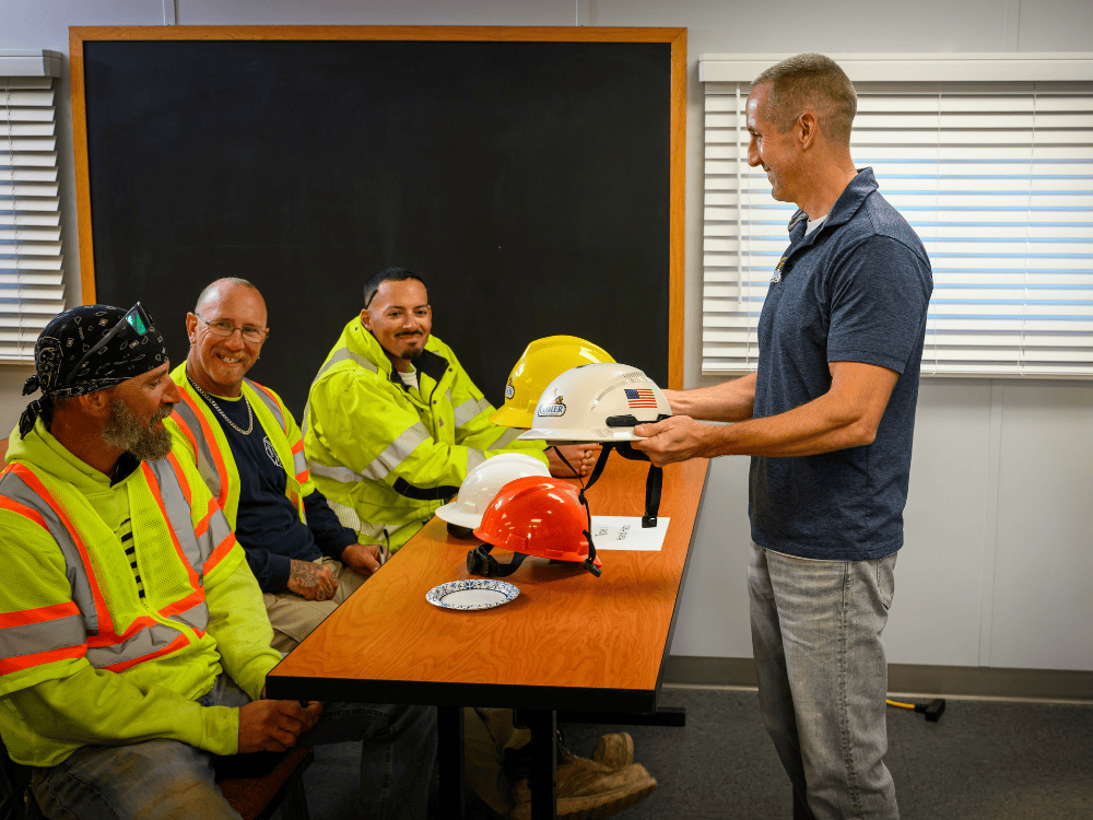 Comer Construction crew members look over the difference between Type I hard hats and Type II safety helmets.