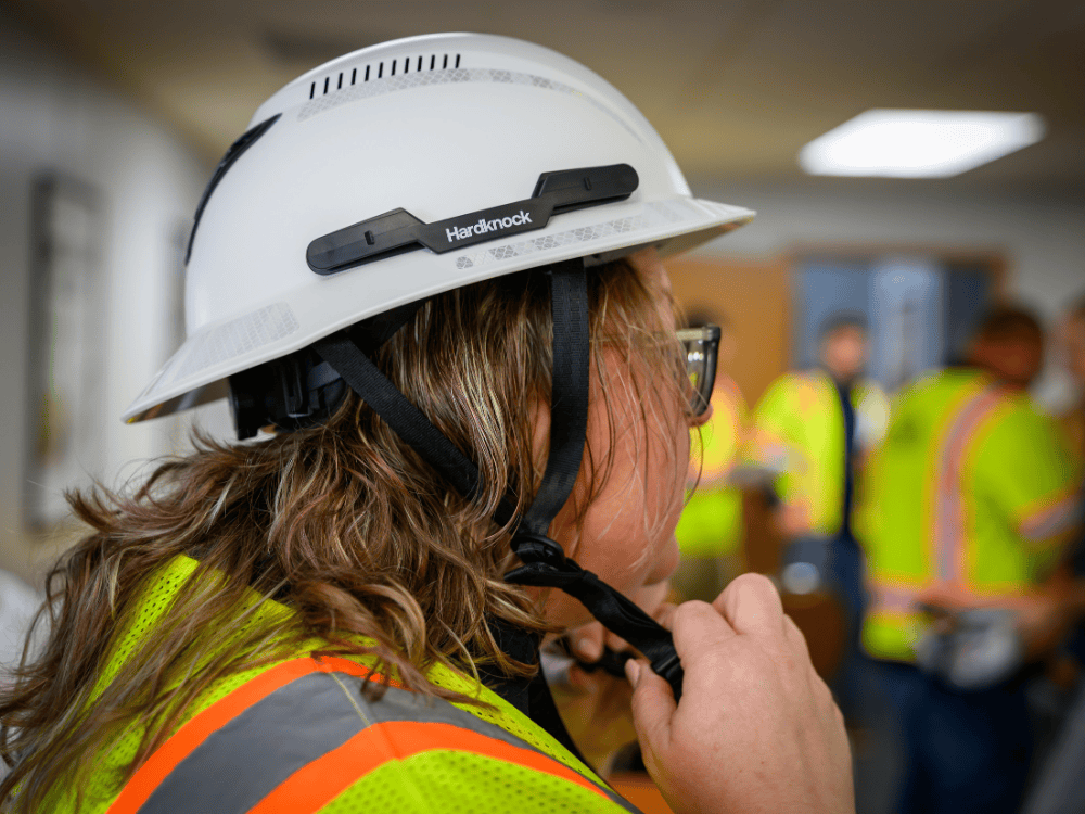 A Comer Construction team member fastens the chin strap on her Type II safety helmet.