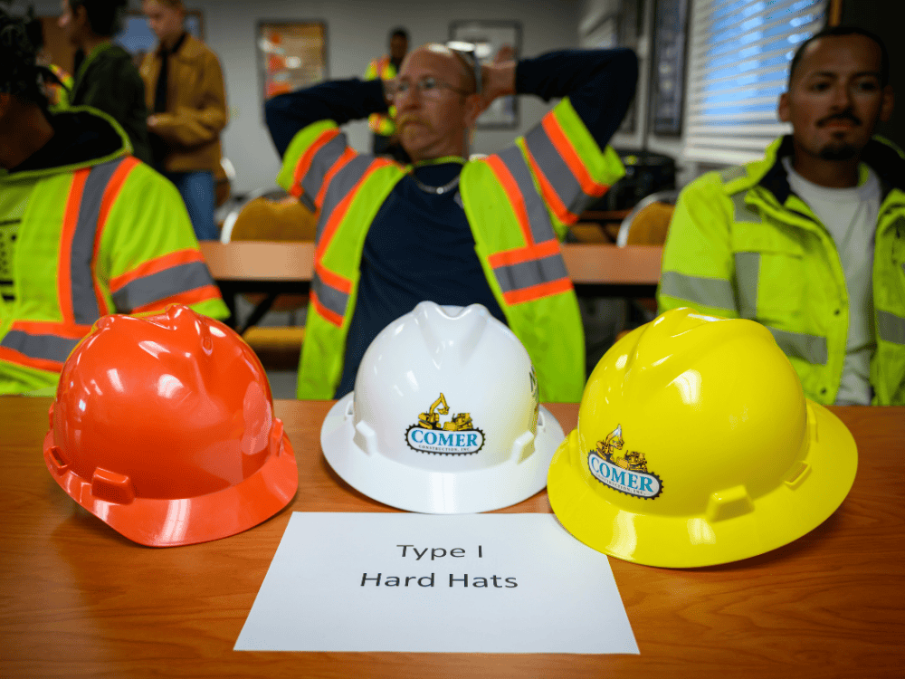 Three traditional Type I hard hats with the Comer Construction logo, the style the team is replacing.